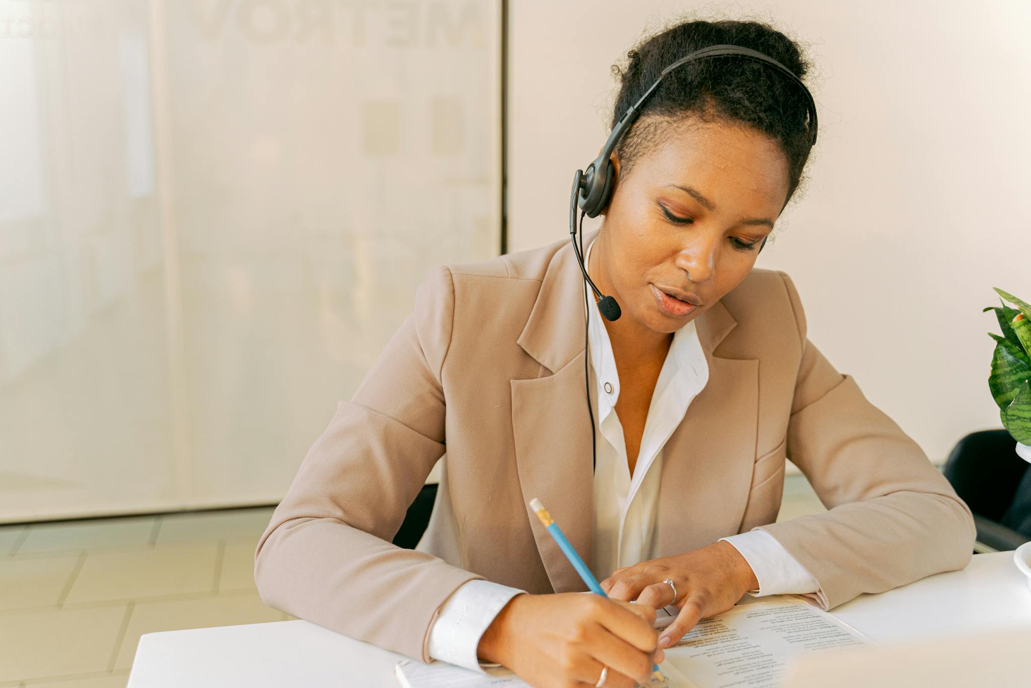 Focused office worker using headset and taking notes in a professional setting.
