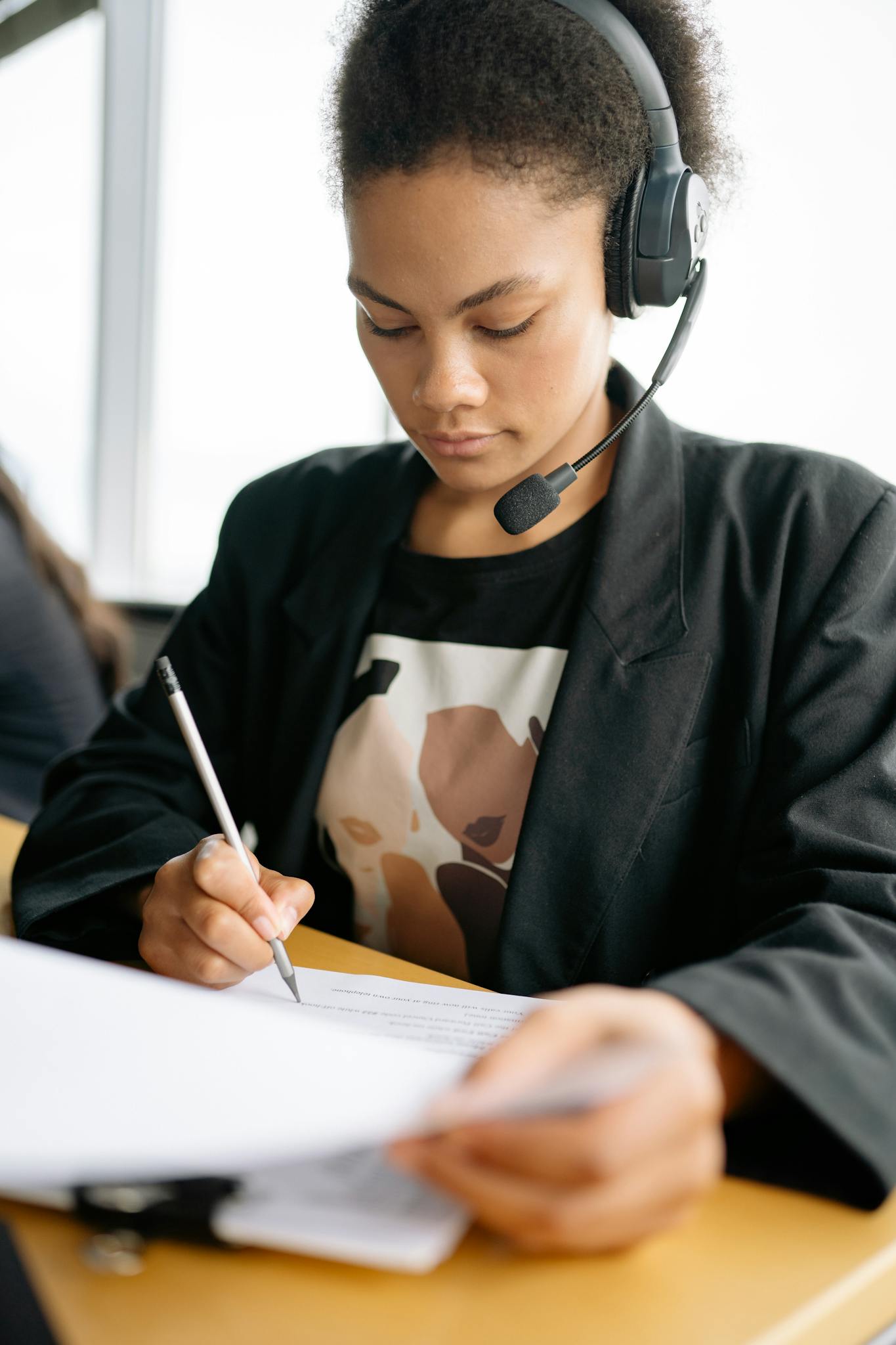 Focused woman working in a call center, writing notes with a headset on.